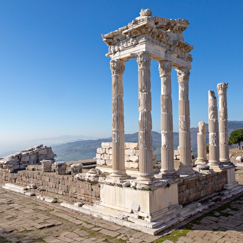Ancient ruins with tall, white stone columns and partially standing structures under a clear blue sky.