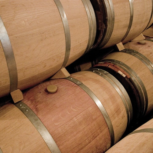 Wooden barrels with metal bands stacked in a storage area, likely for aging wine or spirits.