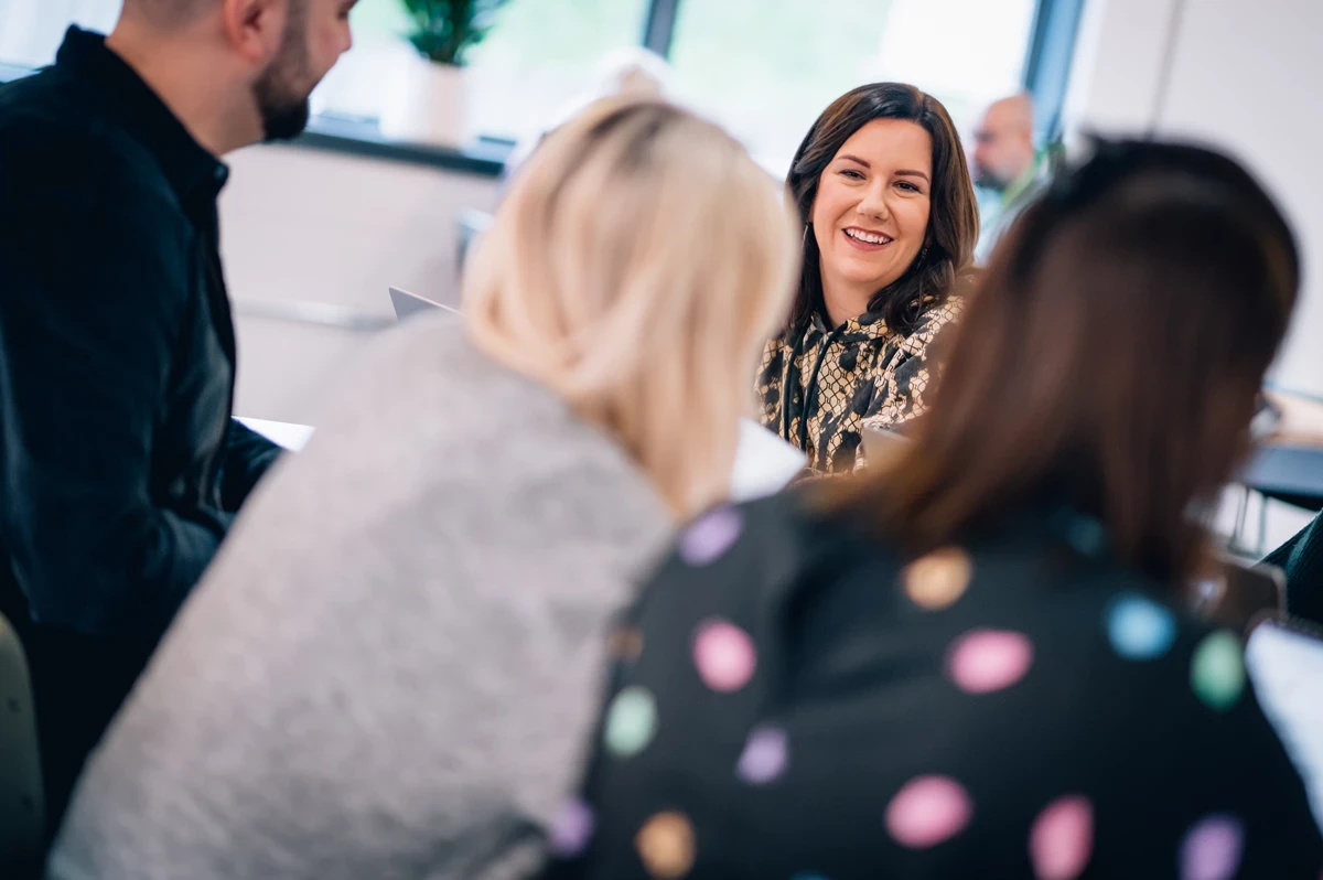 Group of people seated around a table in a bright office space, engaged in discussion with papers in hand.