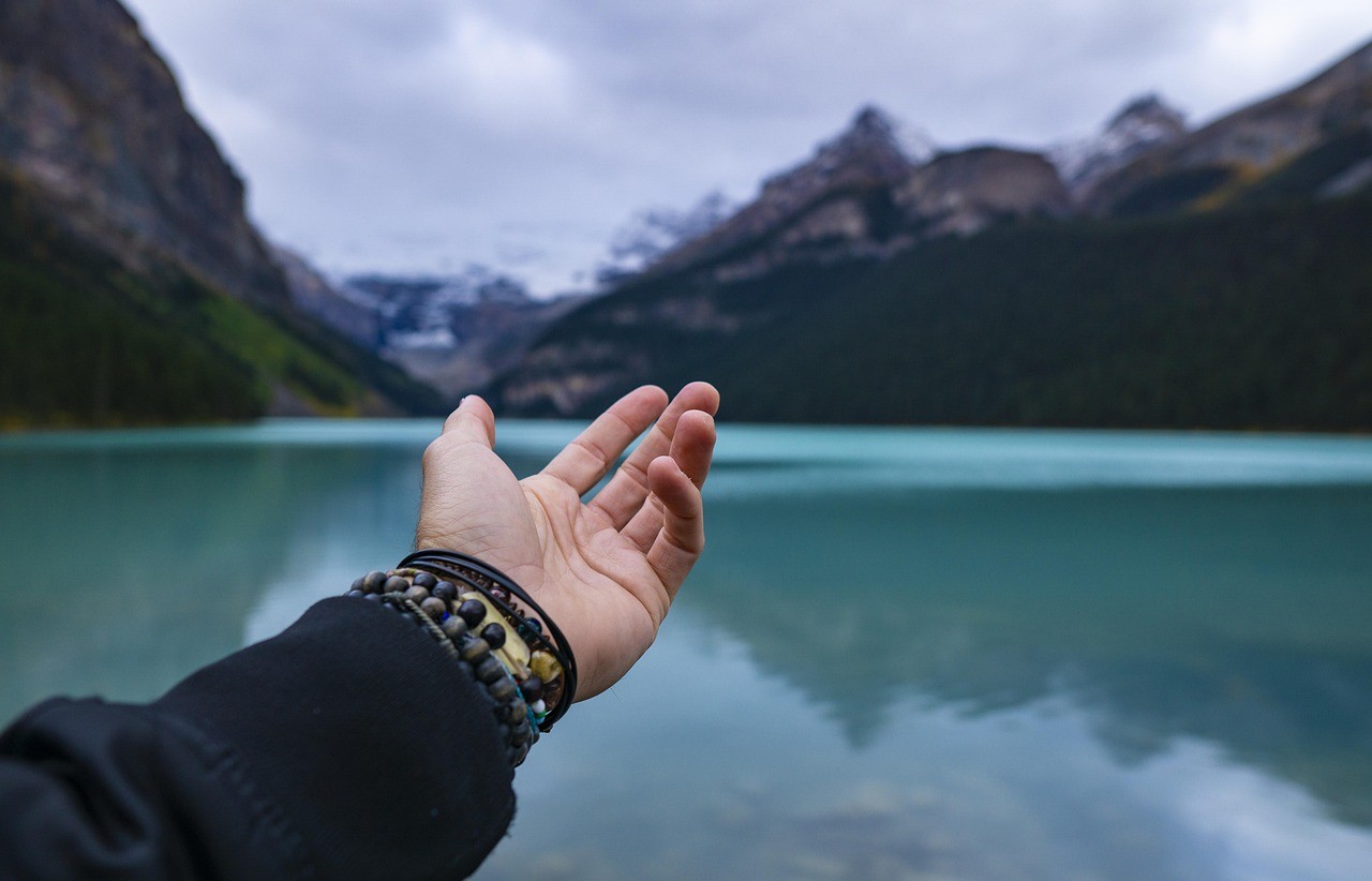 Outstretched hand with mountain lake and forested peaks in the background, showcasing a serene Colorado mountain escape.
