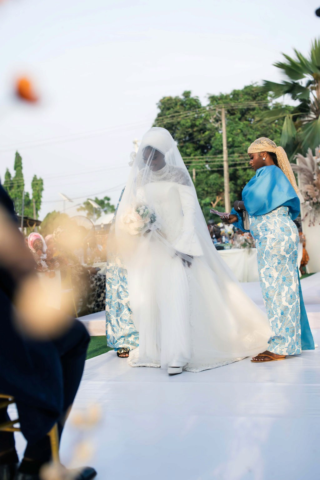 Luxury wedding planned by Victoria Brooks Events in Nigeria with elegant décor and beautiful reception. Groom in a blue suit and bride in a white wedding dress with flowers surrounded by family and friends.