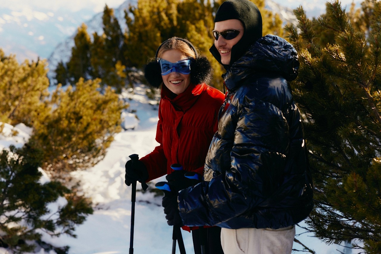 A man and a woman standing on a snowy mountain ridge, overlooking the peaks.