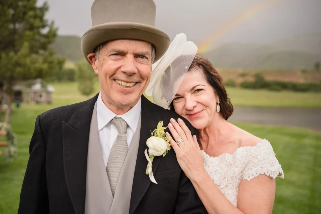 A joyful close-up portrait of the newly married couple smiling together under a faint rainbow at a Chaparral Ranch Wedding.