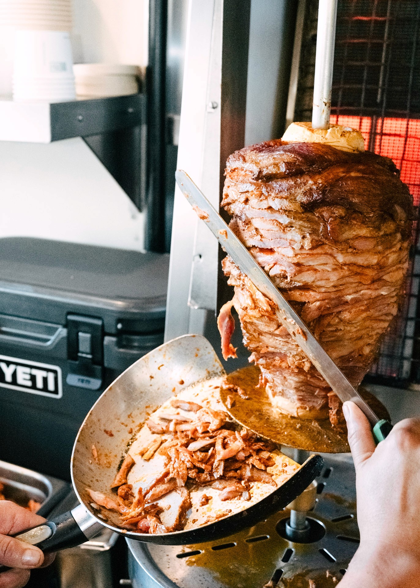 Heritage pork al pastor being carved from the spit into a pan