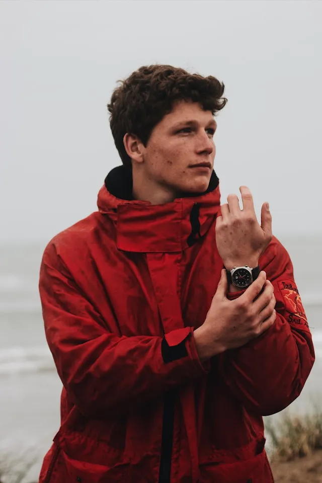Man in a red jacket checking his smartwatch outdoors, focused on tracking performance progress.