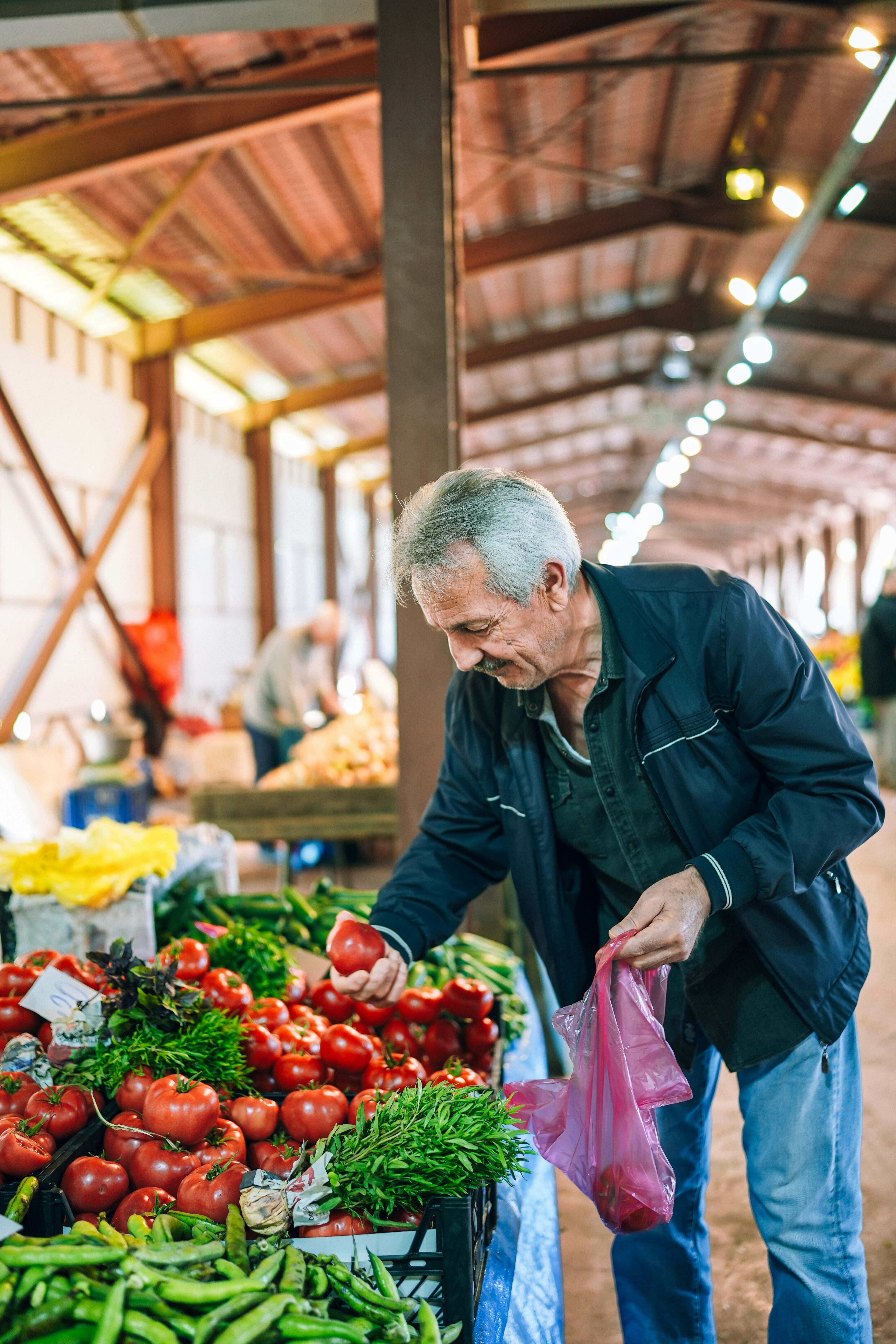 A person examines fresh produce at a vibrant farmer's market, surrounded by colorful fruits and vegetables.