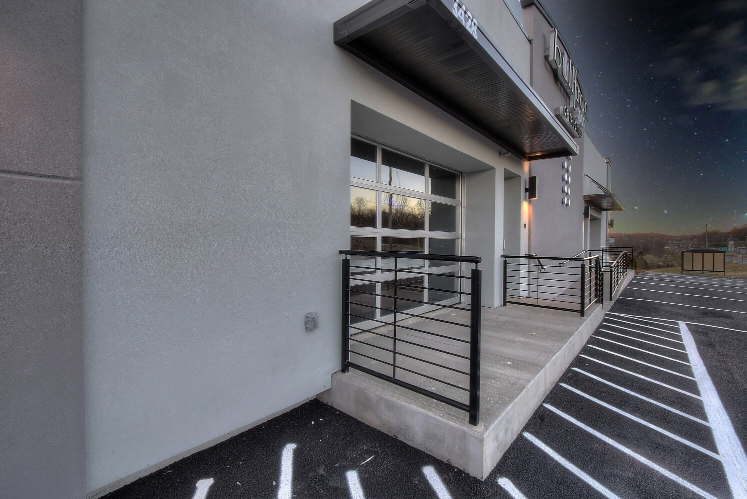 A modern building entrance with large glass doors, featuring a minimalist design and striped pavement.