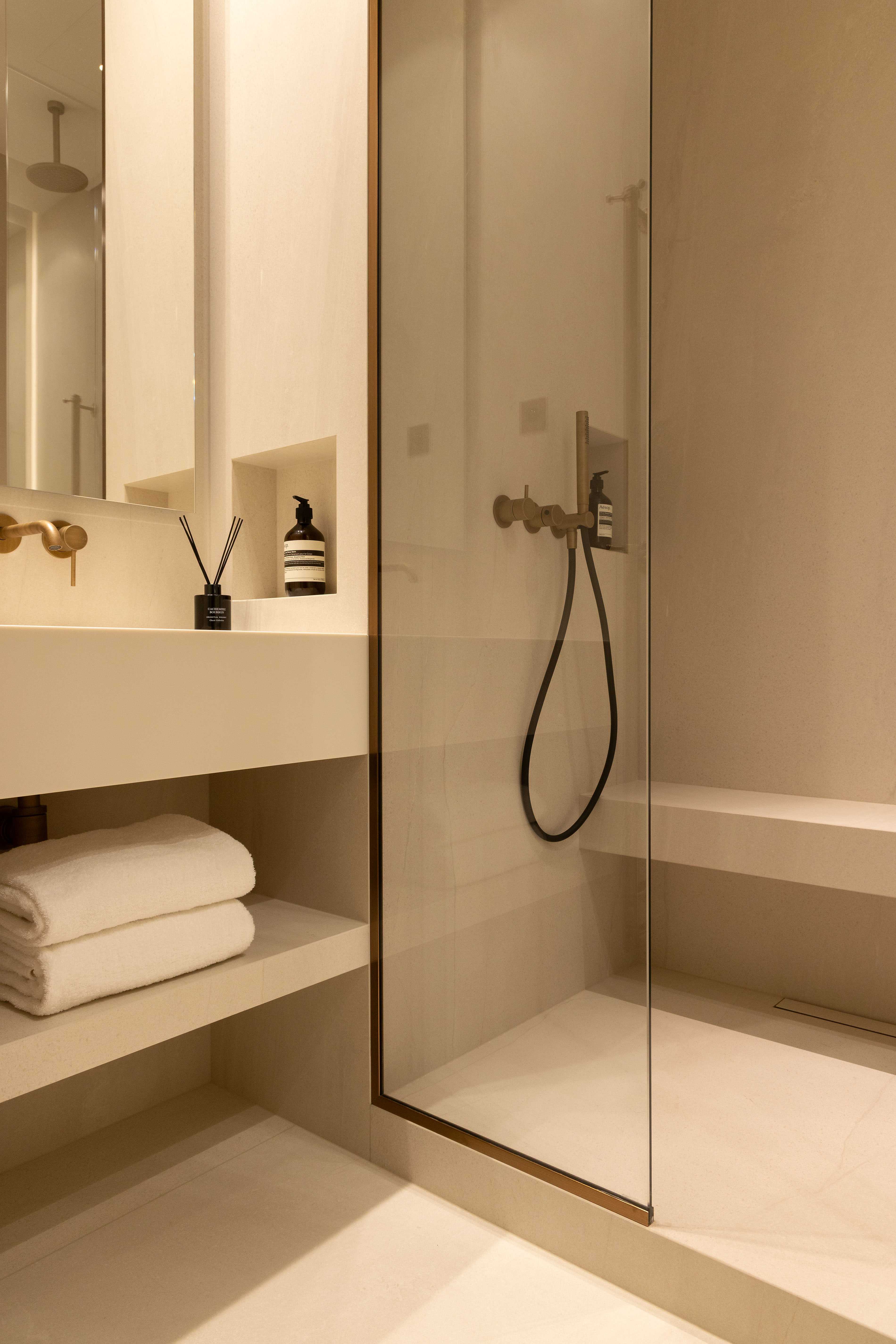 Salle de bain avec vasque, serviettes, douche vitrée avec robinetterie dorée et banc