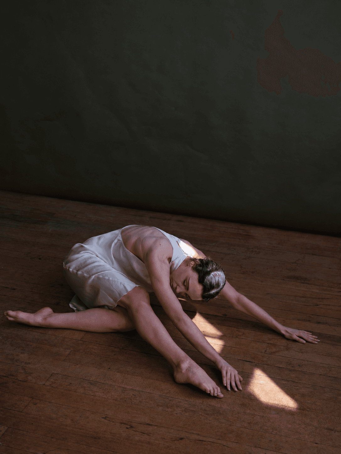 Contemporary dancer stretching across wooden floor in natural light