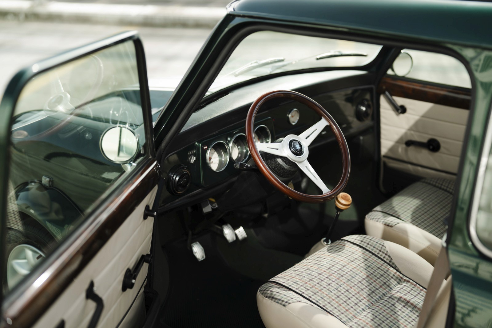 Interior of a vintage car, showcasing the steering wheel, seats, and open door with a scenic background.