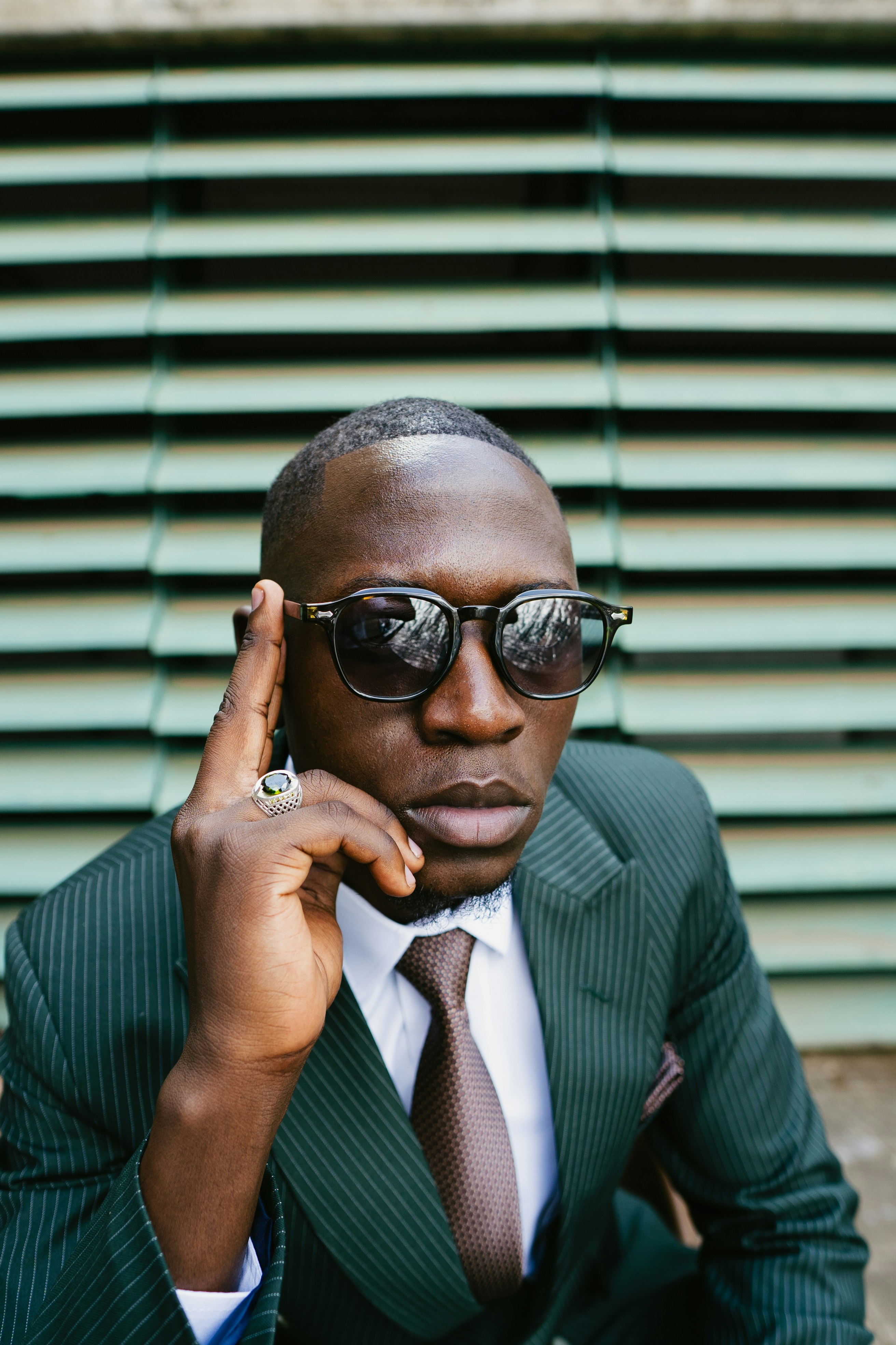Man in suit and sunglasses with hand on temple.