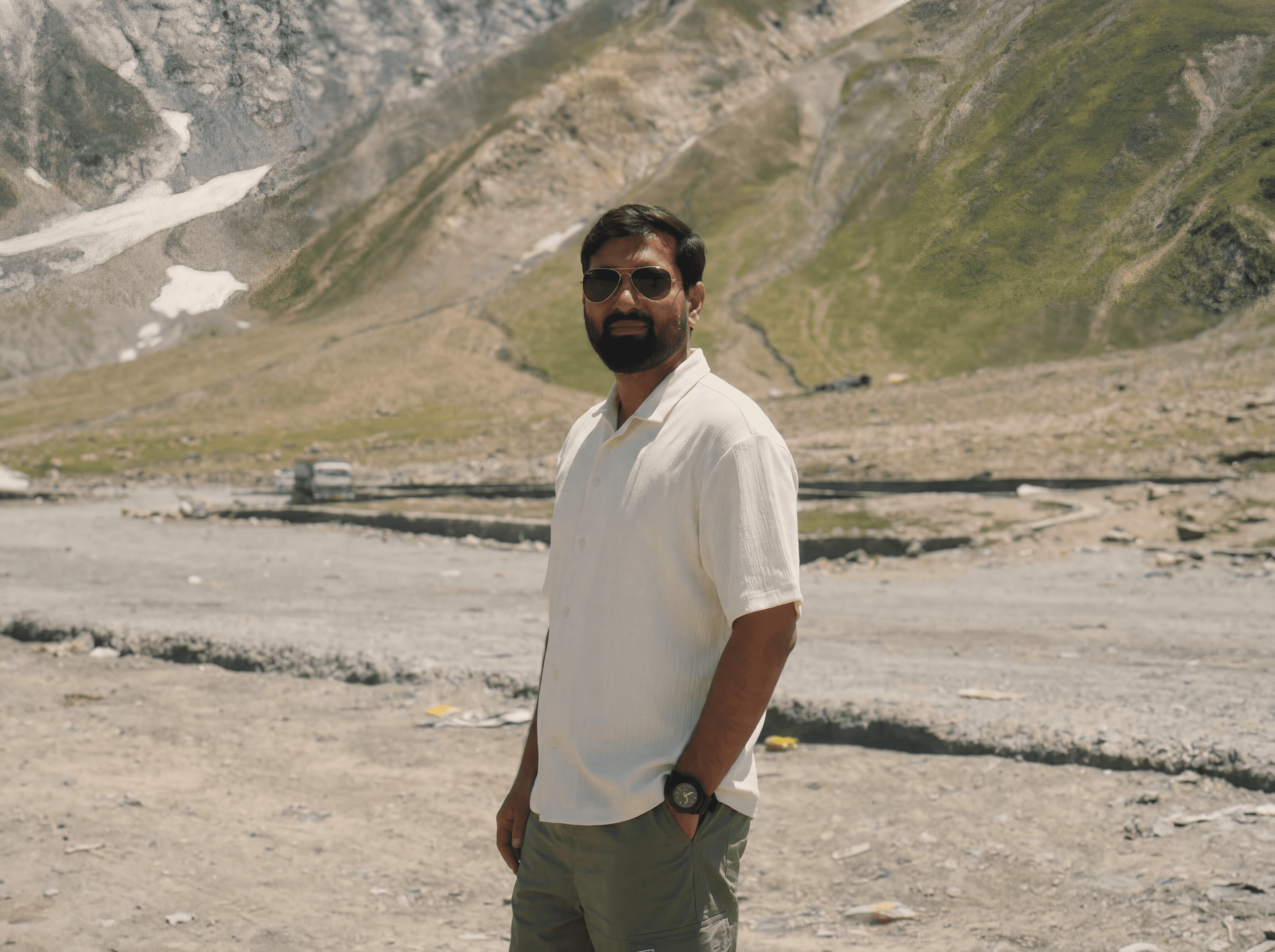A smiling man with short hair stands with arms crossed, wearing a dark shirt against a neutral background.