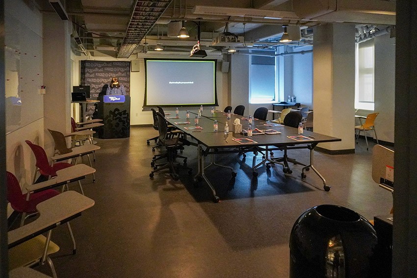 Presentation office with a table and chairs around it, chairs near the left wall, and an image projected by a projector on the wall in the back
