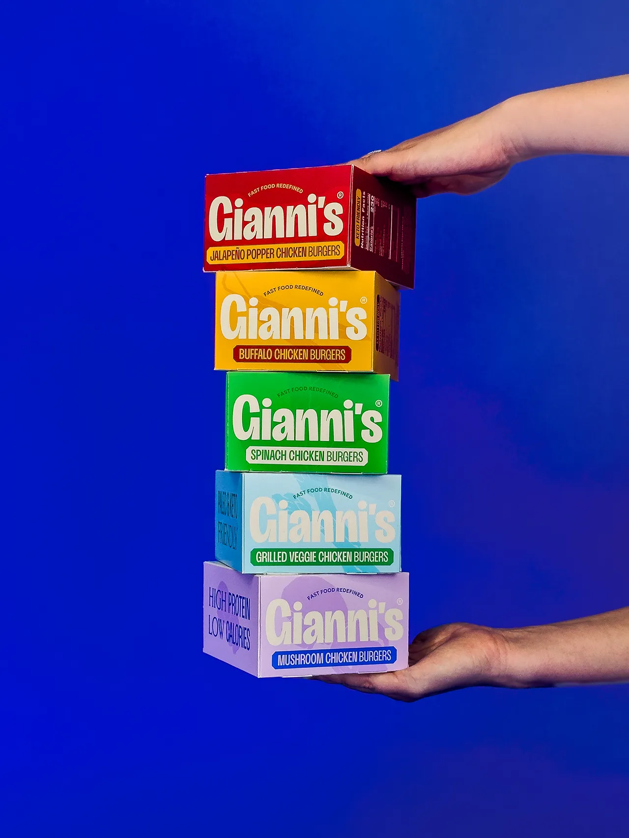 Hands holding a vertical stack of colorful Gianni’s chicken burger packages