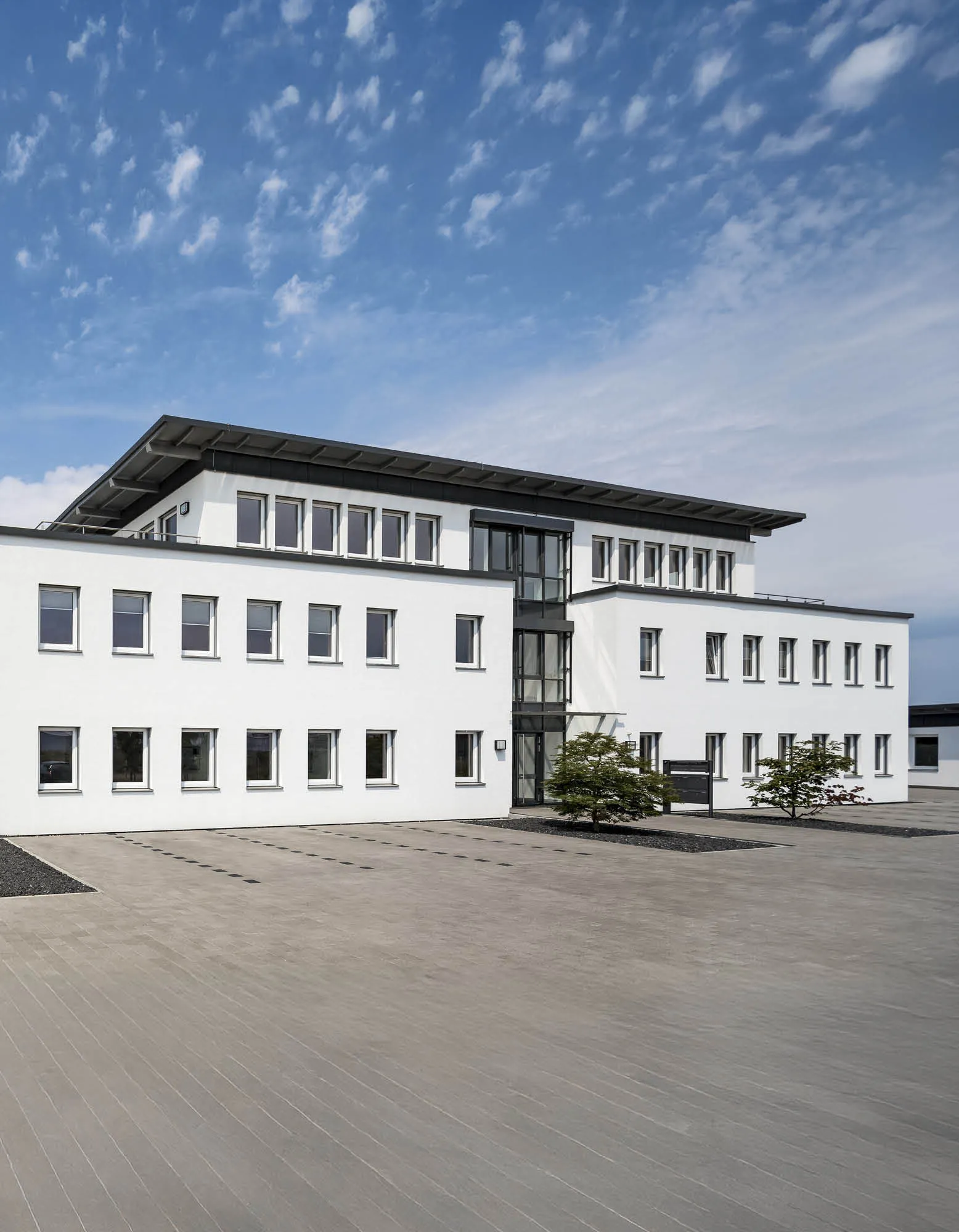 Modernes weißes Bürogebäude mit vielen Fenstern vor einem blauen Himmel mit vereinzelten Wolken.