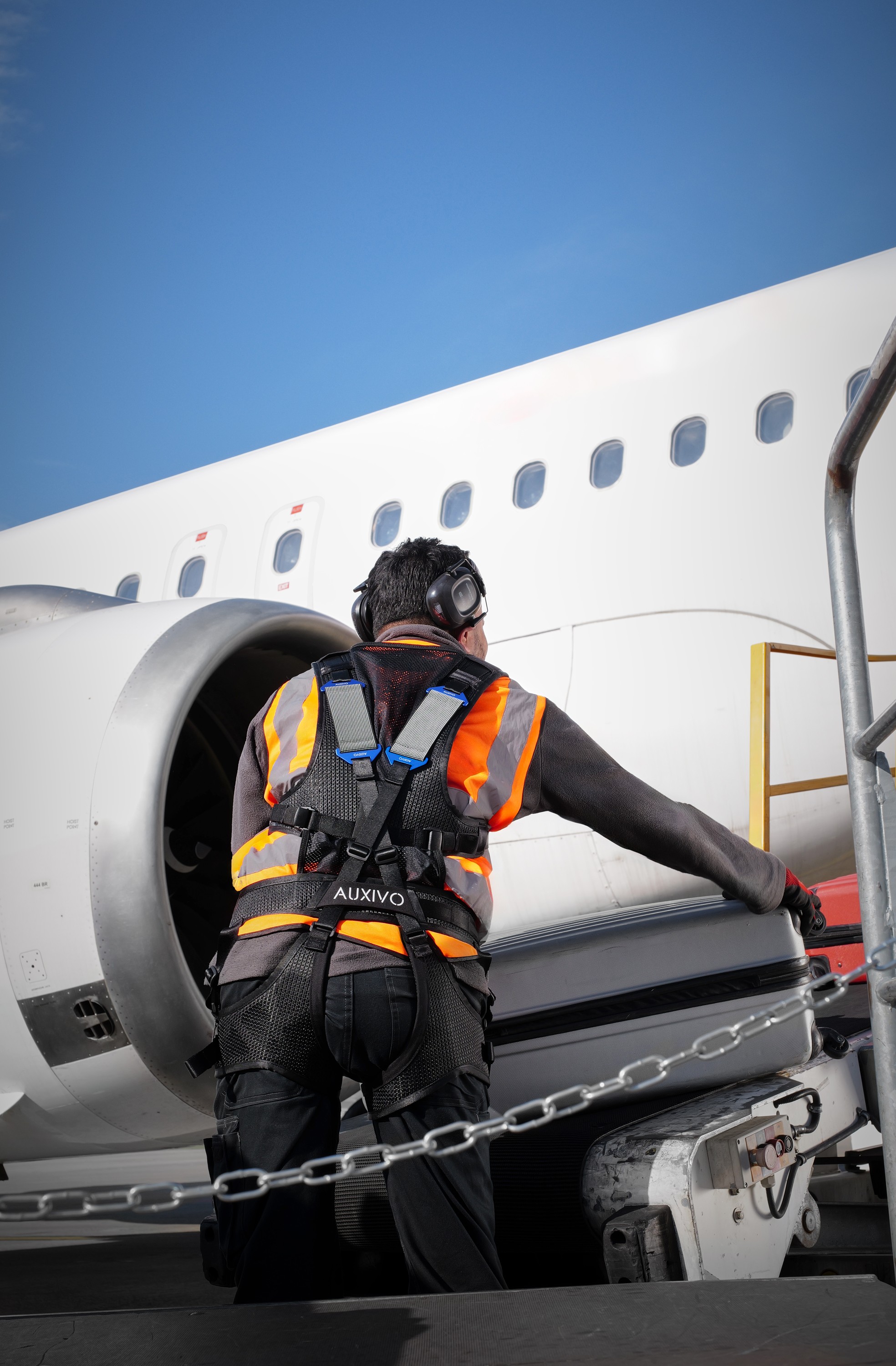 Airport agent wearing the Auxivo LiftSuit exoskeleton handling loads on a conveyor, reducing lower back strain and the risk of injury.