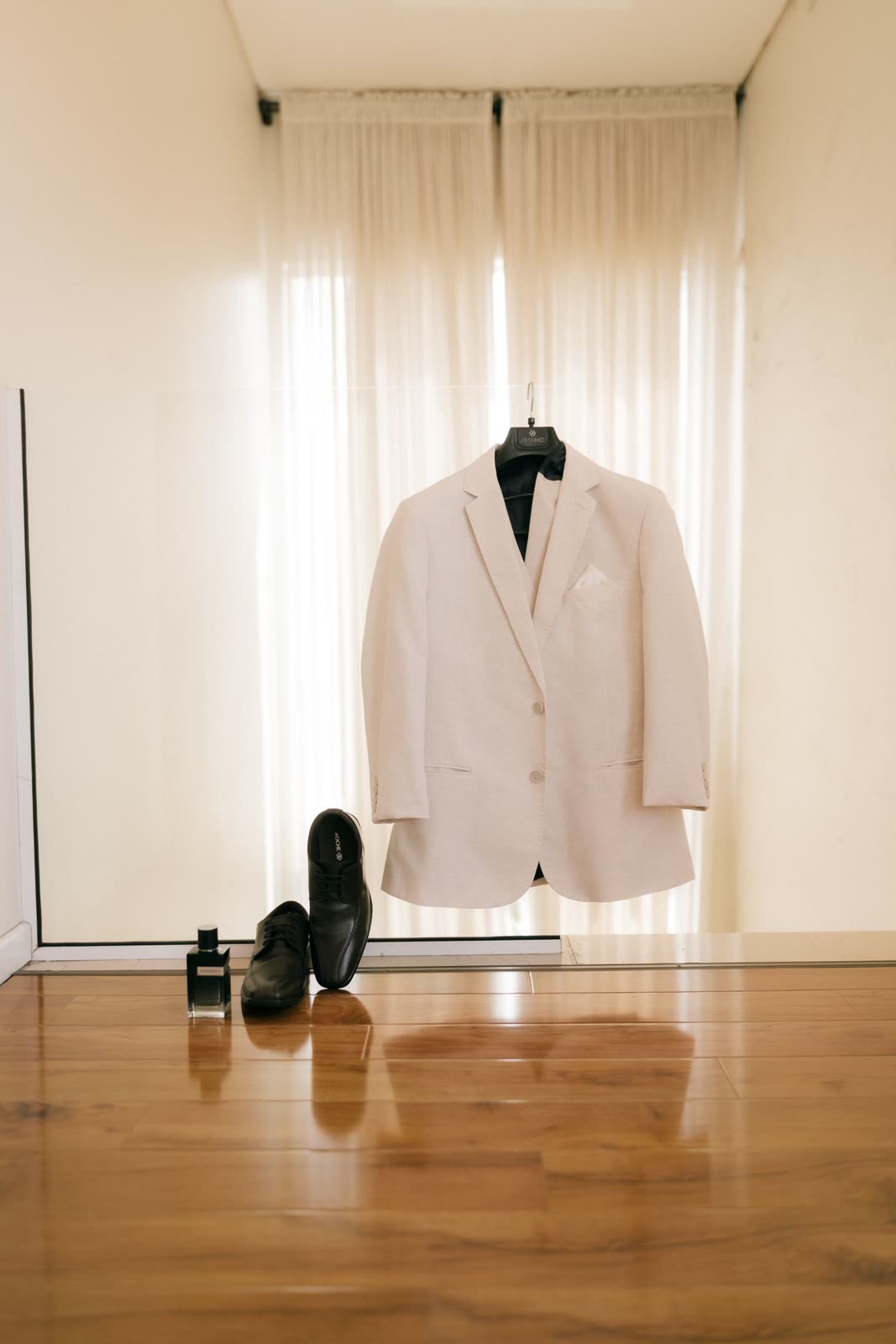 White suit jacket on a hanger above a pair of black shoes in a bright room