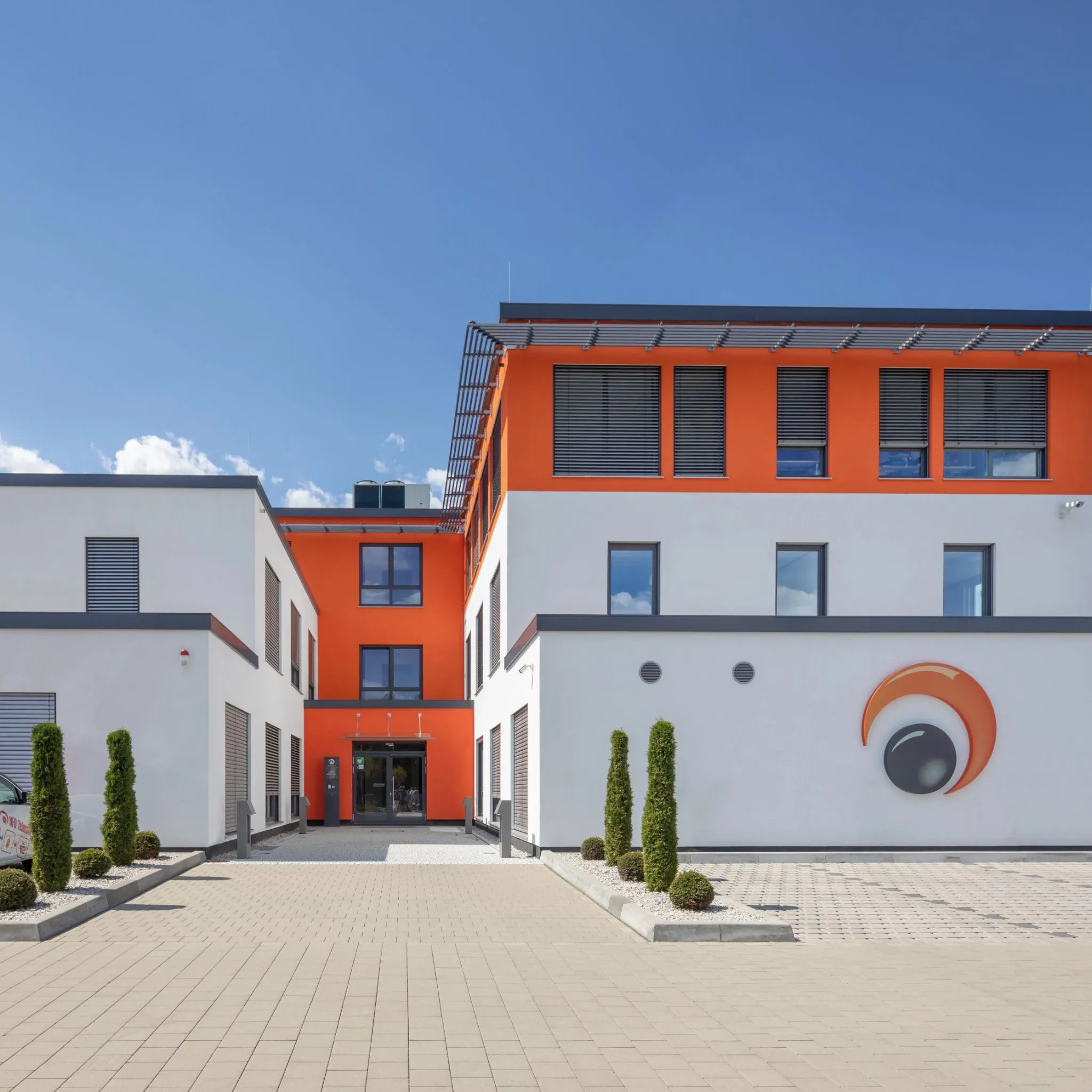 Moderne Bürofassade mit orangefarbenen Akzenten und einem stilisierten Auge als Logo.