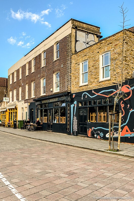 A smiling man with curly hair is sitting at a desk, looking at the camera, with a laptop and a lamp in the background.