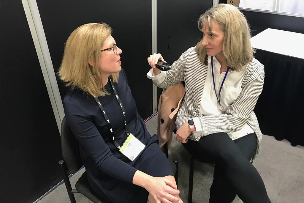 Two women sitting and engaged in conversation in a professional setting, with a black backdrop.