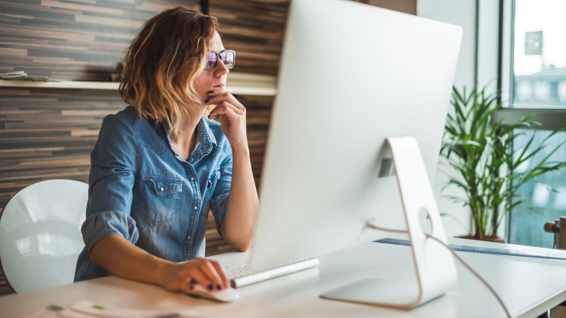 A woman pauses with her hand to her chin, carefully reviewing what's on her monitor