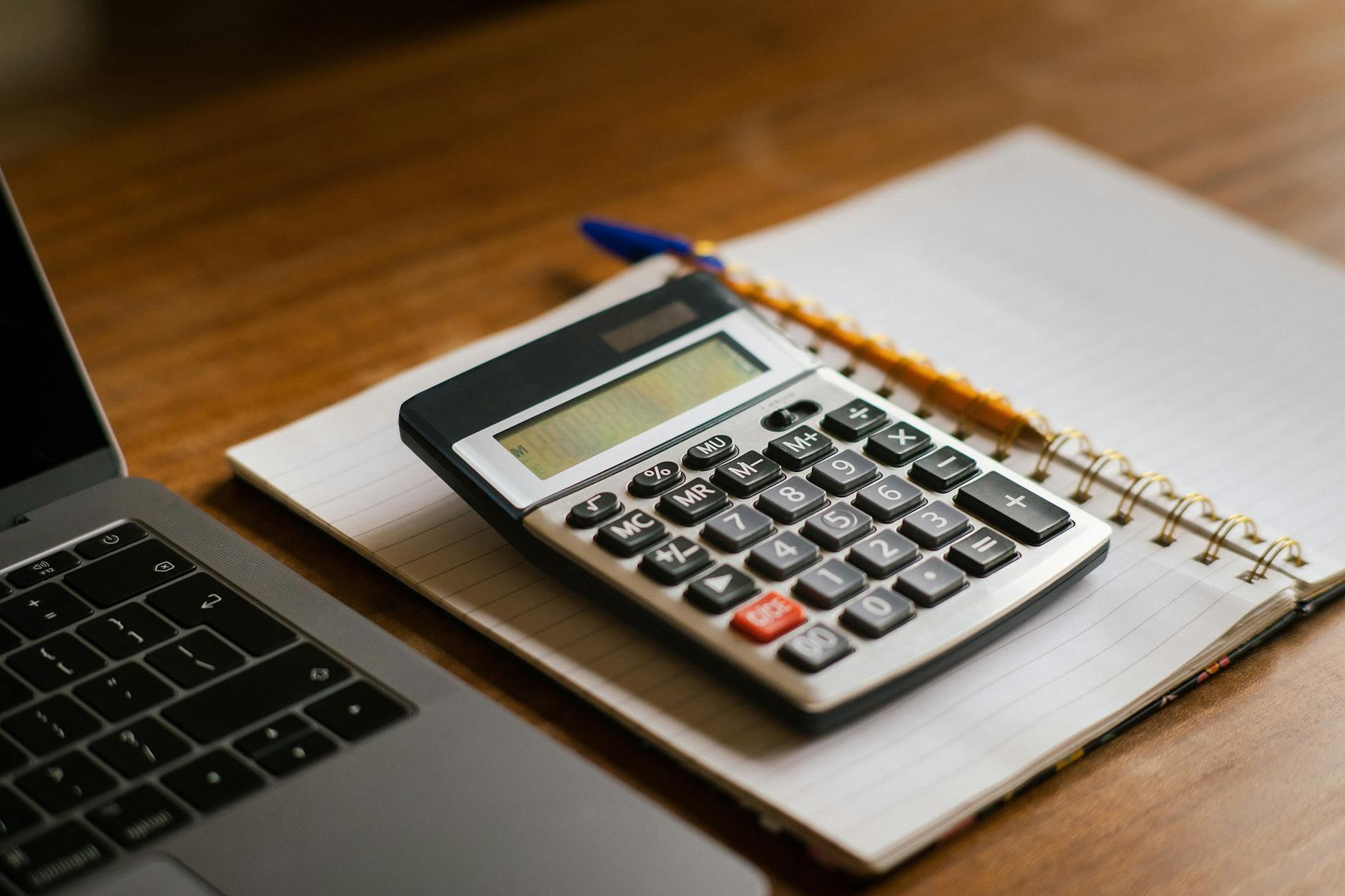 A close-up of a hand using a calculator next to a spreadsheet showing a budget comparison of software fees.