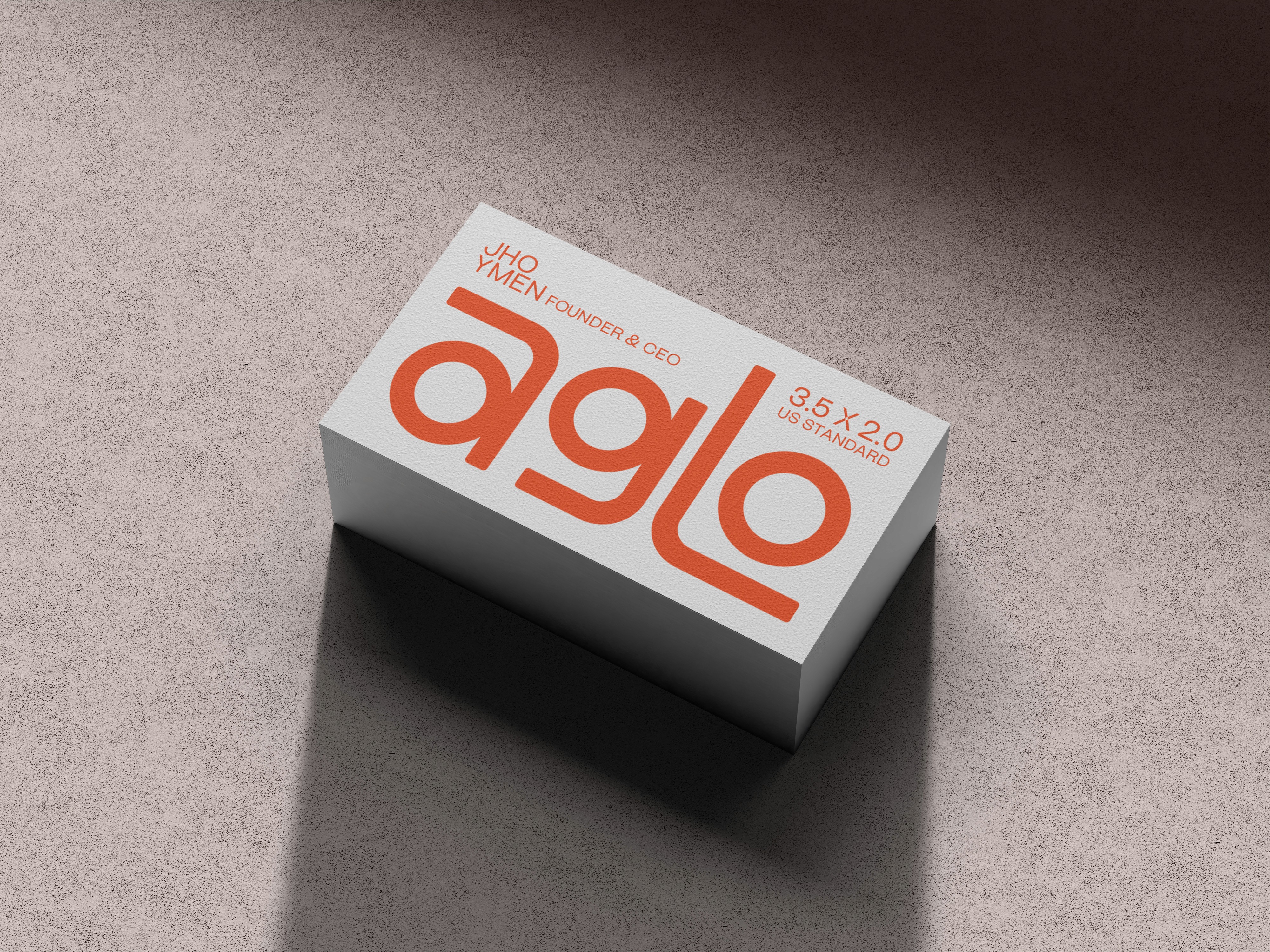 A high-angle perspective mockup of a thick, white business card featuring the bold orange logo "aglo" and "Founder & CEO" details, resting on a textured grey surface with sharp, realistic shadows.