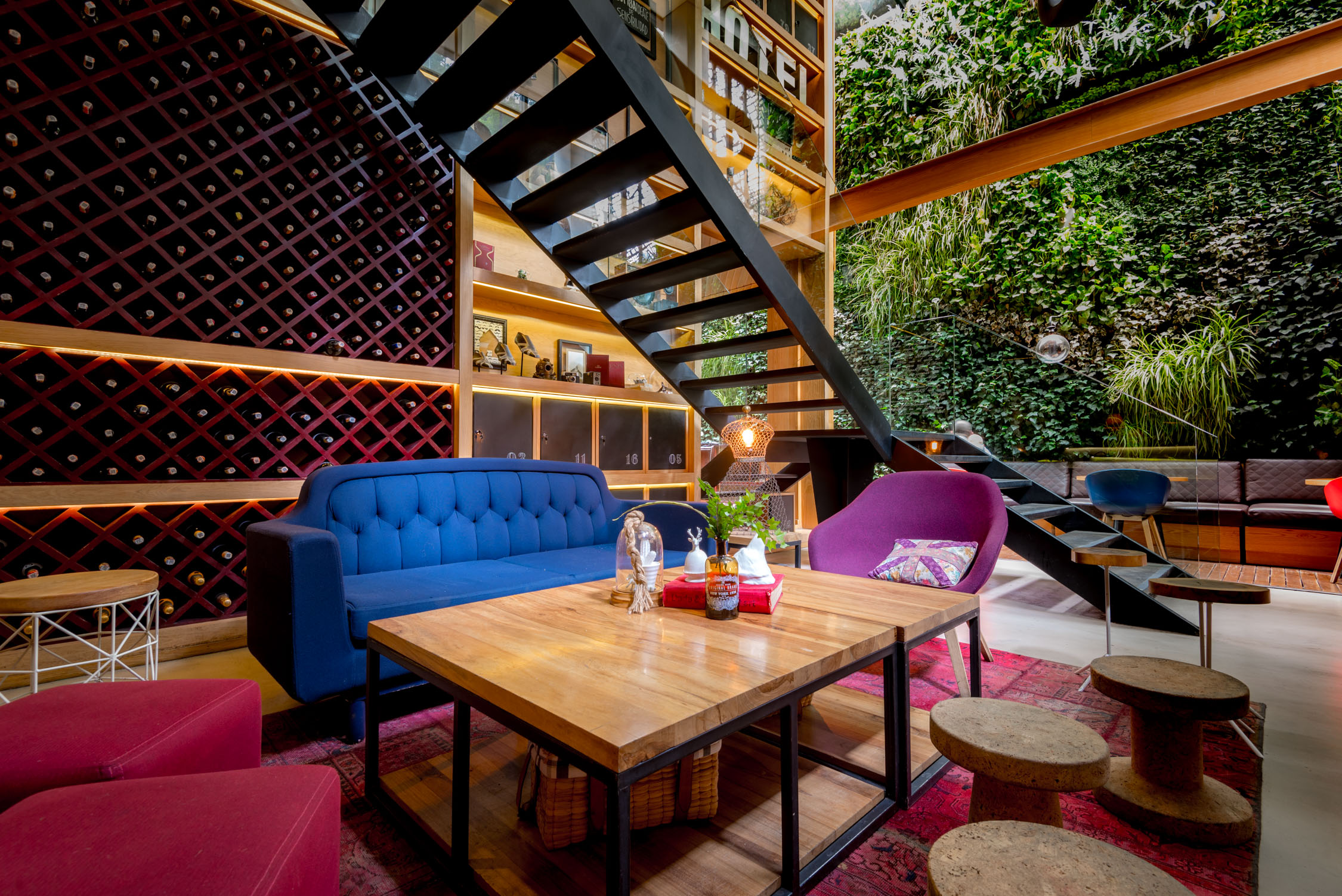 A modern wine cellar interior features a wooden table with glasses and bottles, a blue sofa, and a large wall of wine.