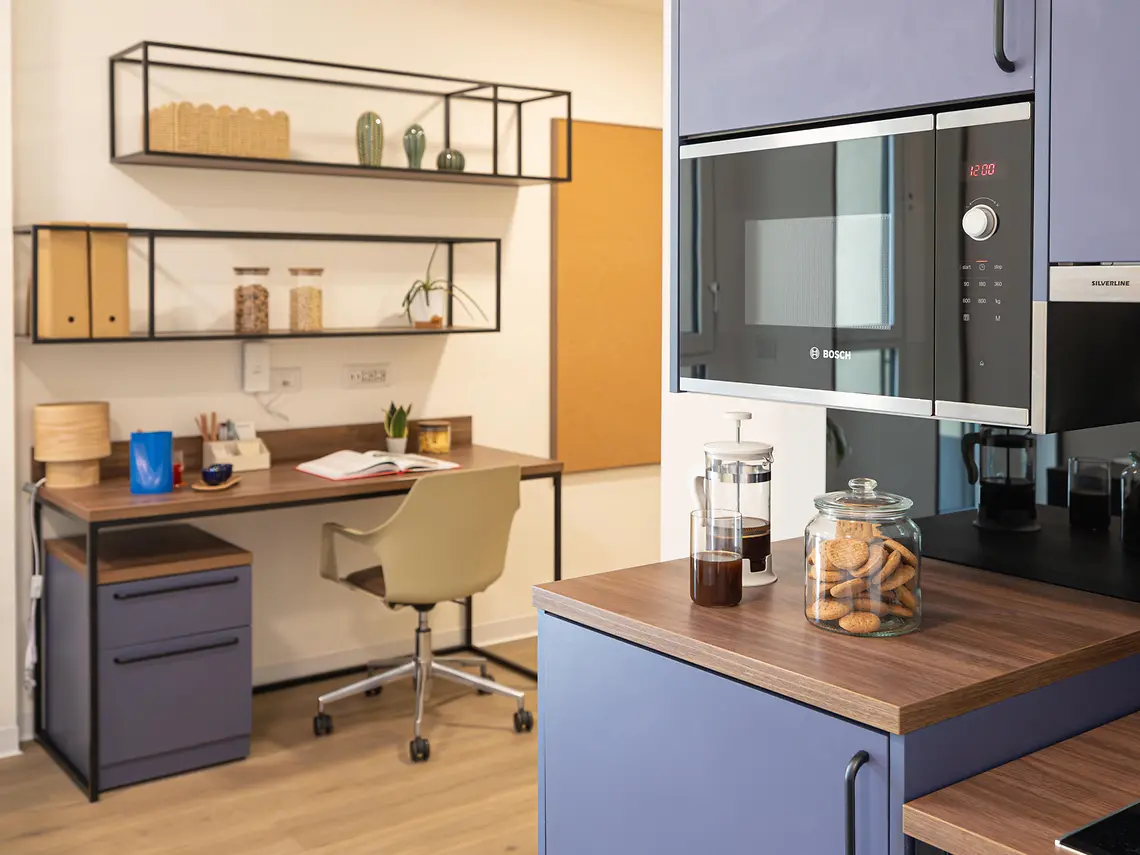 Study desk beside the fitted kitchen in a Bologna student studio, with shelving and Bosch appliances