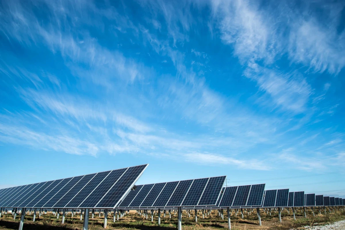 Solar panels in a field beneath a cloudy blue sky.