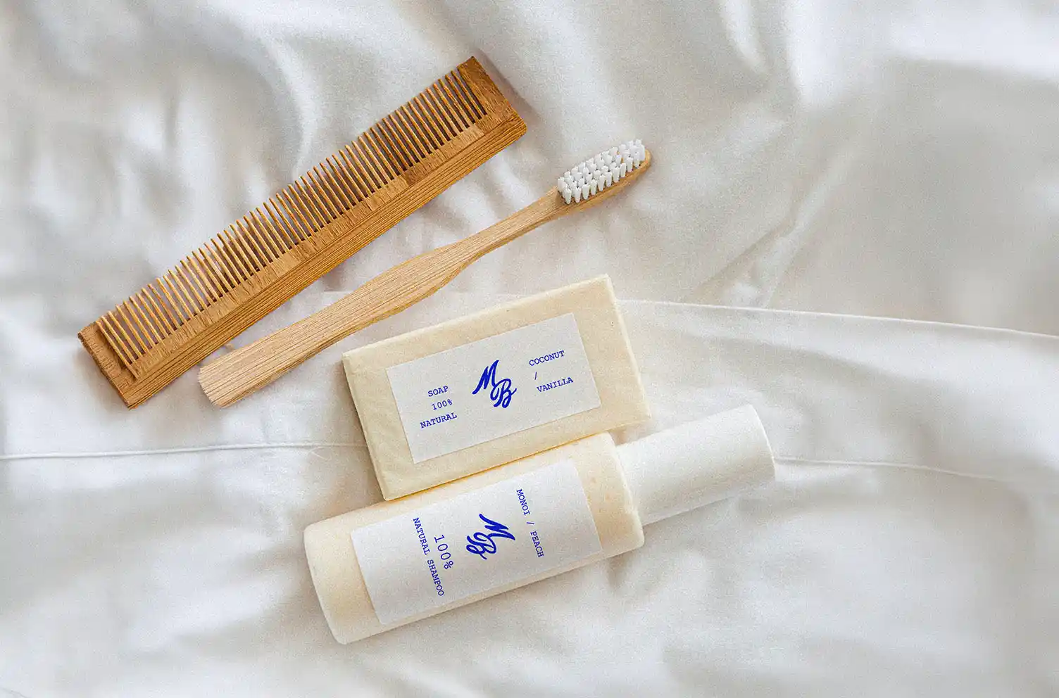 Flat lay des amenities Marble Blue sur linge blanc : savon naturel et shampoing emballés papier crème brandés MB, peigne et brosse à dents en bambou.