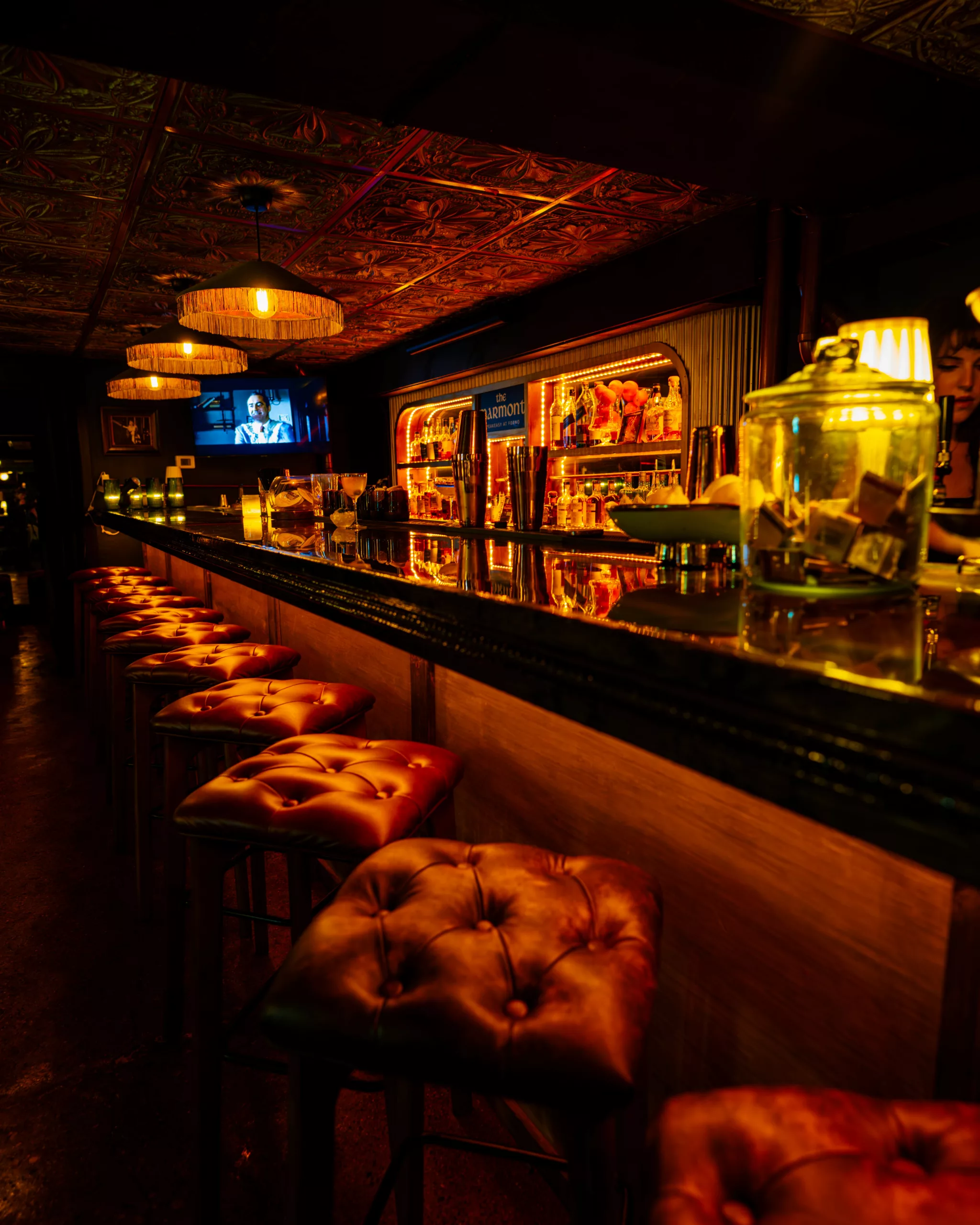 Dim speakeasy bar with tufted stools and warm lights in Marmont at Forno Speakeasy, Forno Kitchen + Bar