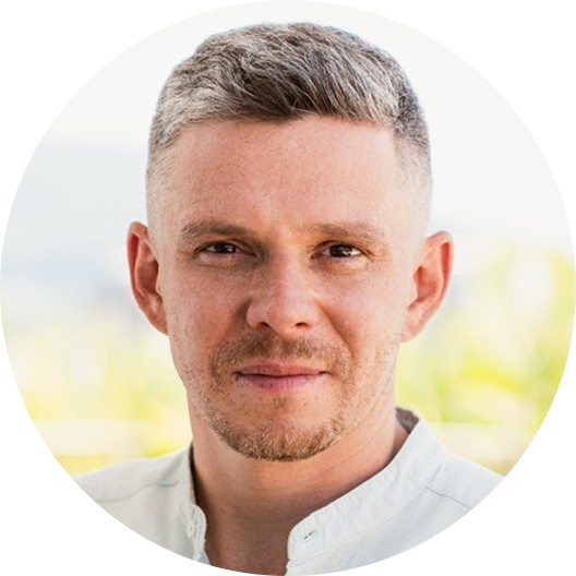 Editorial portrait of a young man with wavy hair in a knit sweater, looking over his shoulder in soft light.
