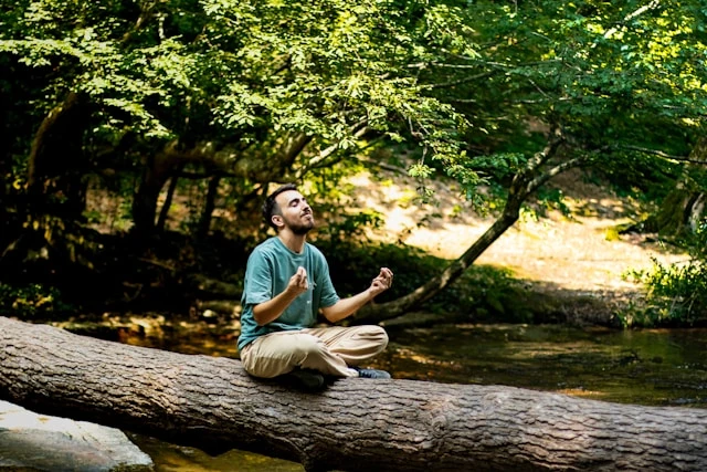 Man standing outdoors in a green forest clearing with sunlight shining through trees, looking uplifted.