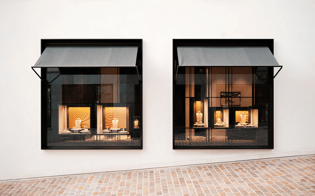 Two storefront display windows with jewelry under black awnings, brick flooring.