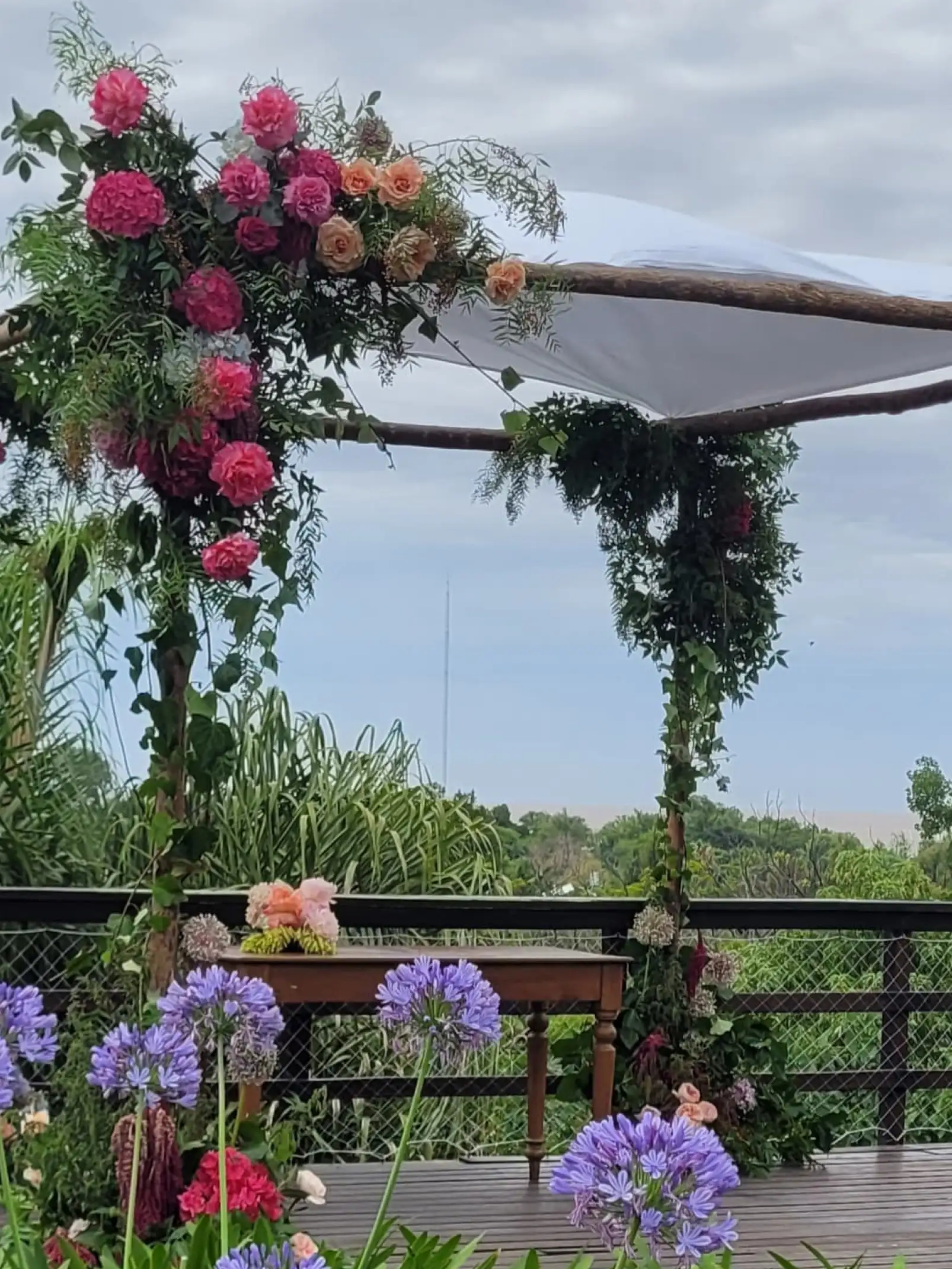 Arco decorado con flores rosadas y durazno sobre fondo verde para ceremonia natural, creando un ambiente romántico y fresco.