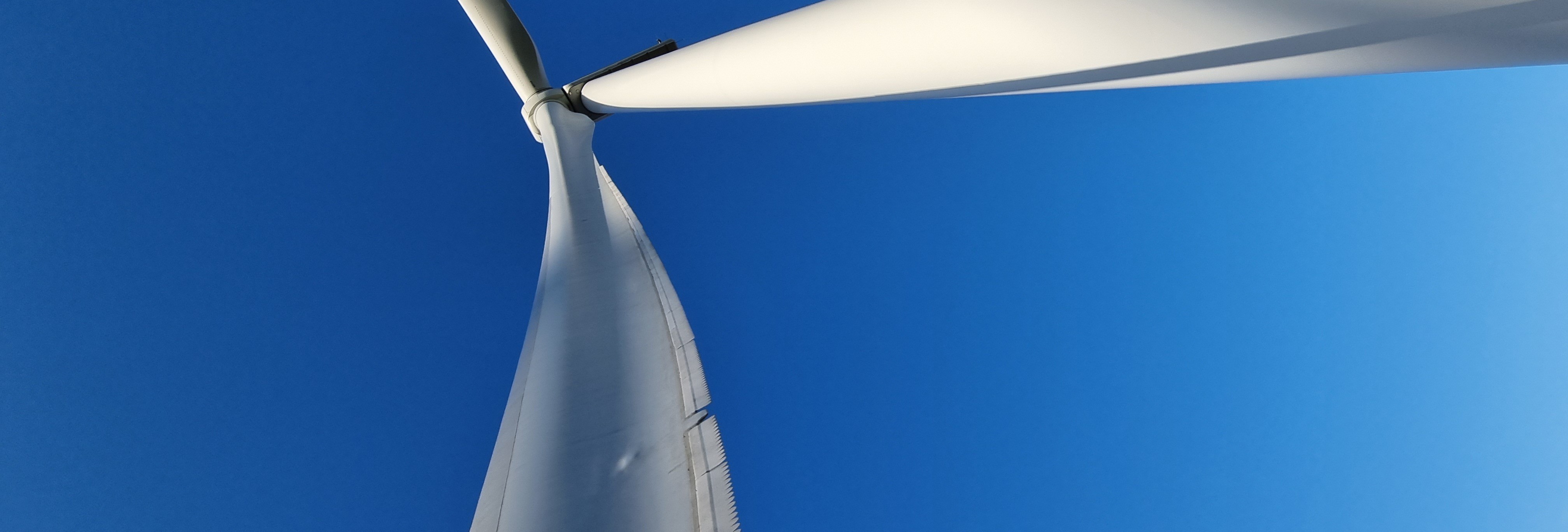 Looking up at a wind turbine rotor against a clear blue sky, with MuteSkin on the blade trailing edge