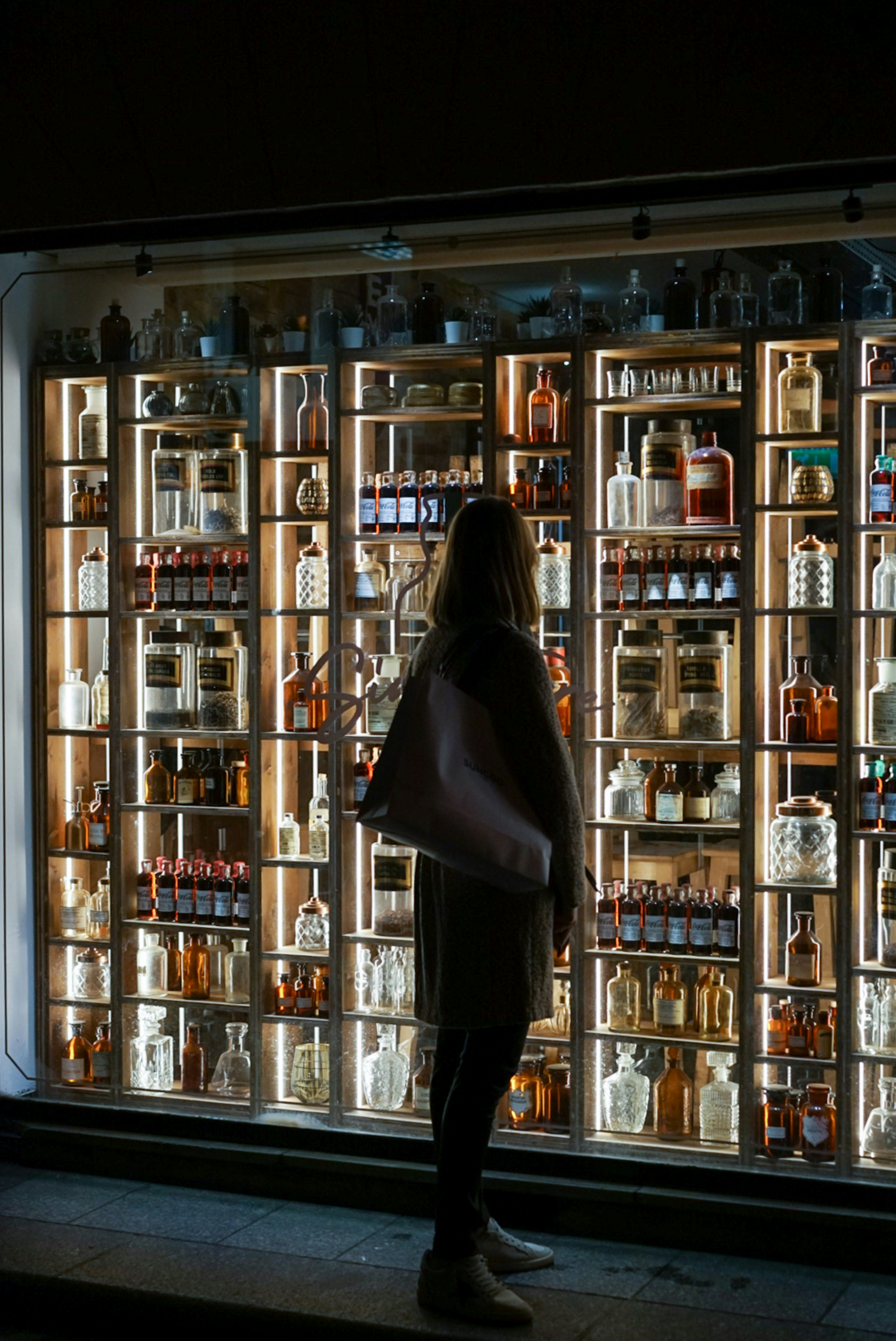 A silhouette of a person standing in front of a wall filled with books, illuminated softly from behind.