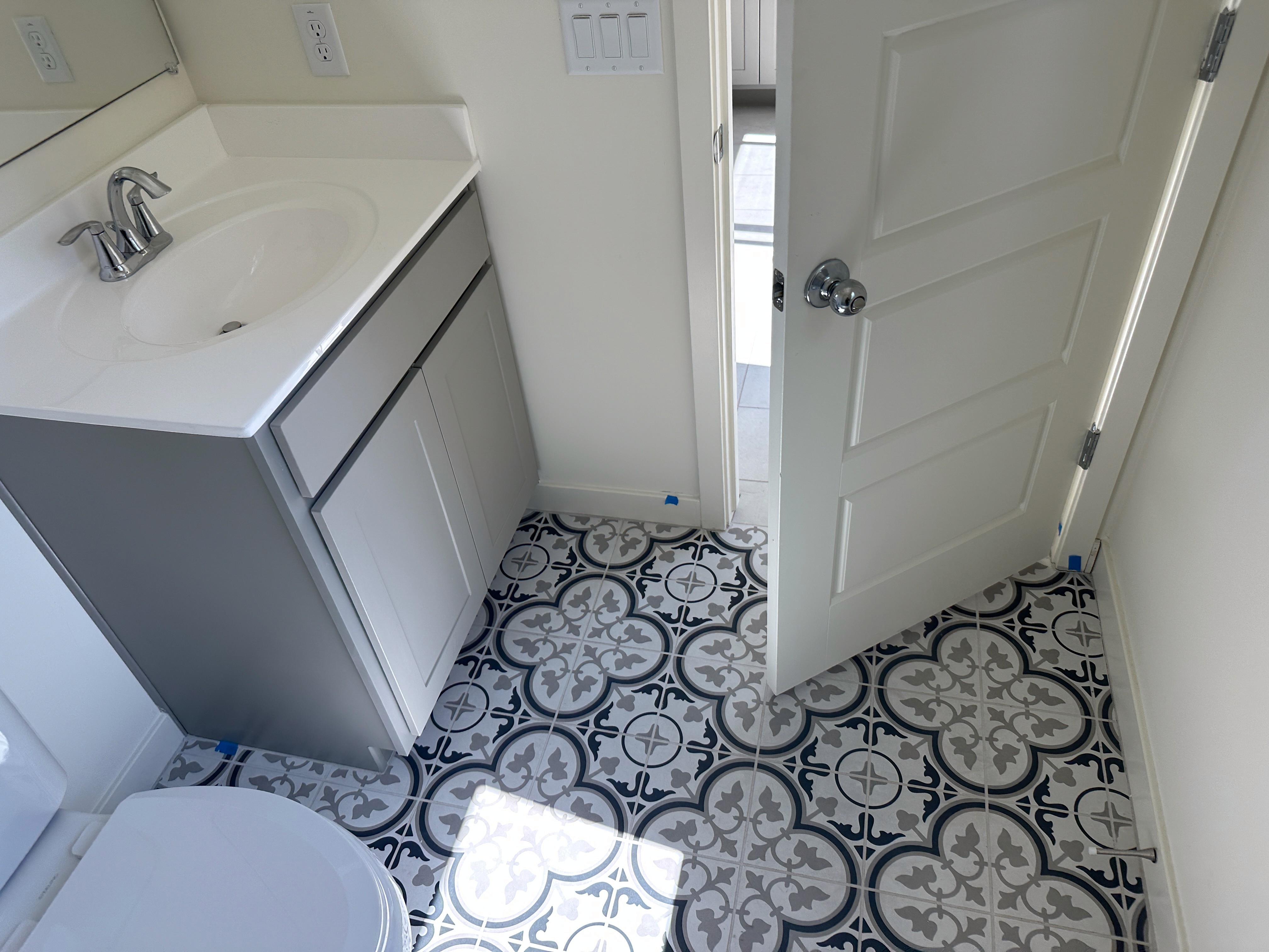 Modern bathroom with patterned tile flooring, single sink vanity, and open door in a new home under construction.