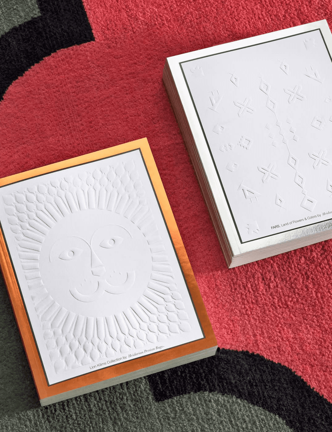 Embossed luxury book covers with geometric and sun-face motifs displayed on a patterned carpet, showcasing refined print design and premium material craftsmanship.
