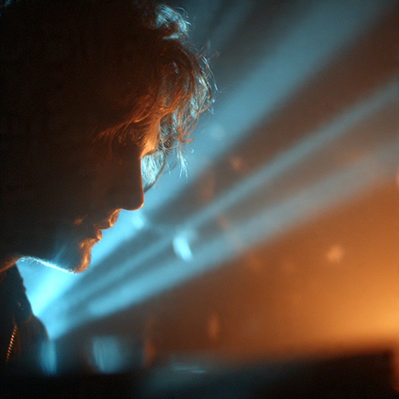 A profile of a person in dramatic lighting. The left side is illuminated by cool blue light, while warm orange light shines from the right, creating a moody atmosphere.