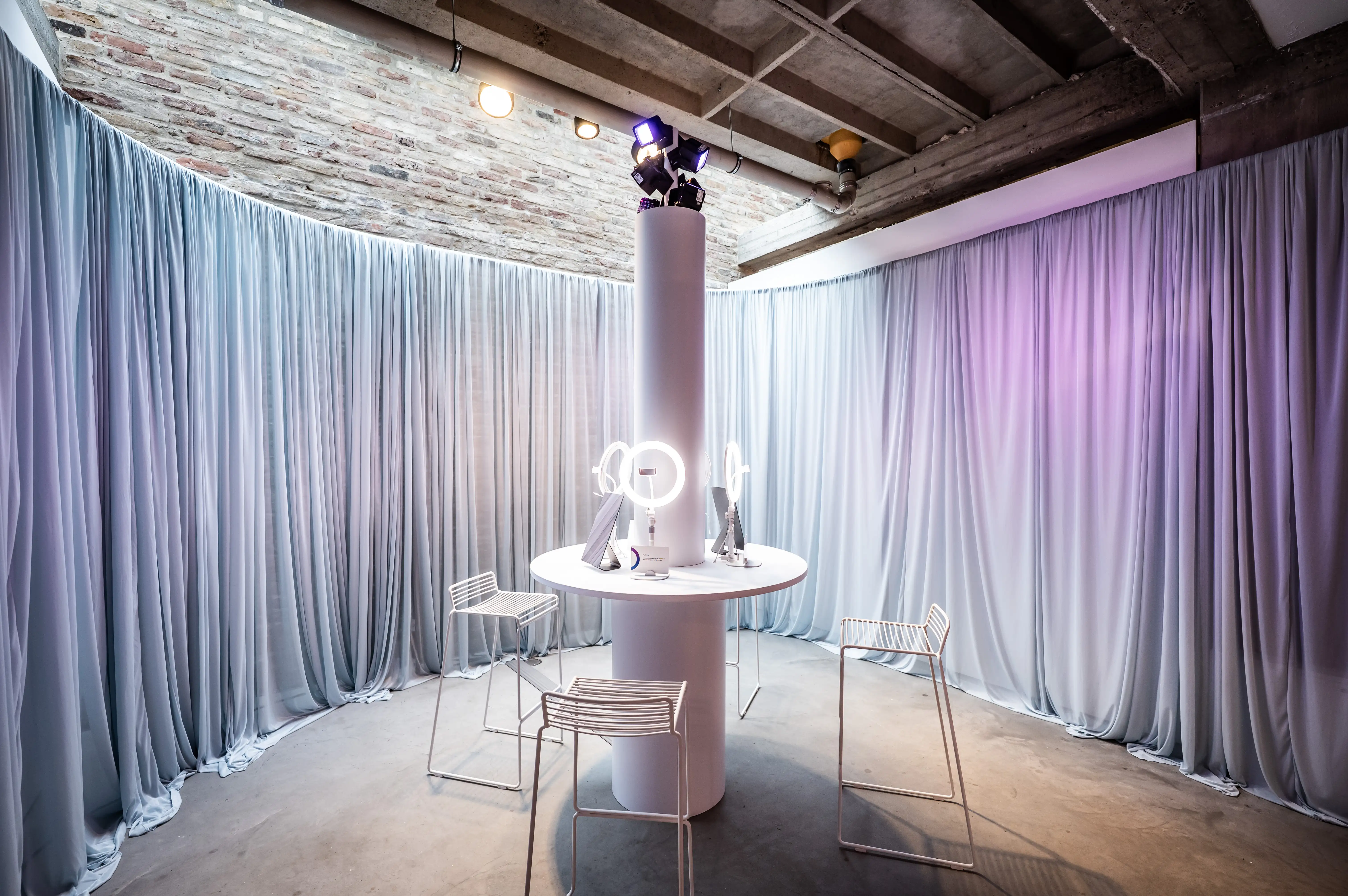 Photo studio with round white table, ring lights and grey curtain walls in purple light.