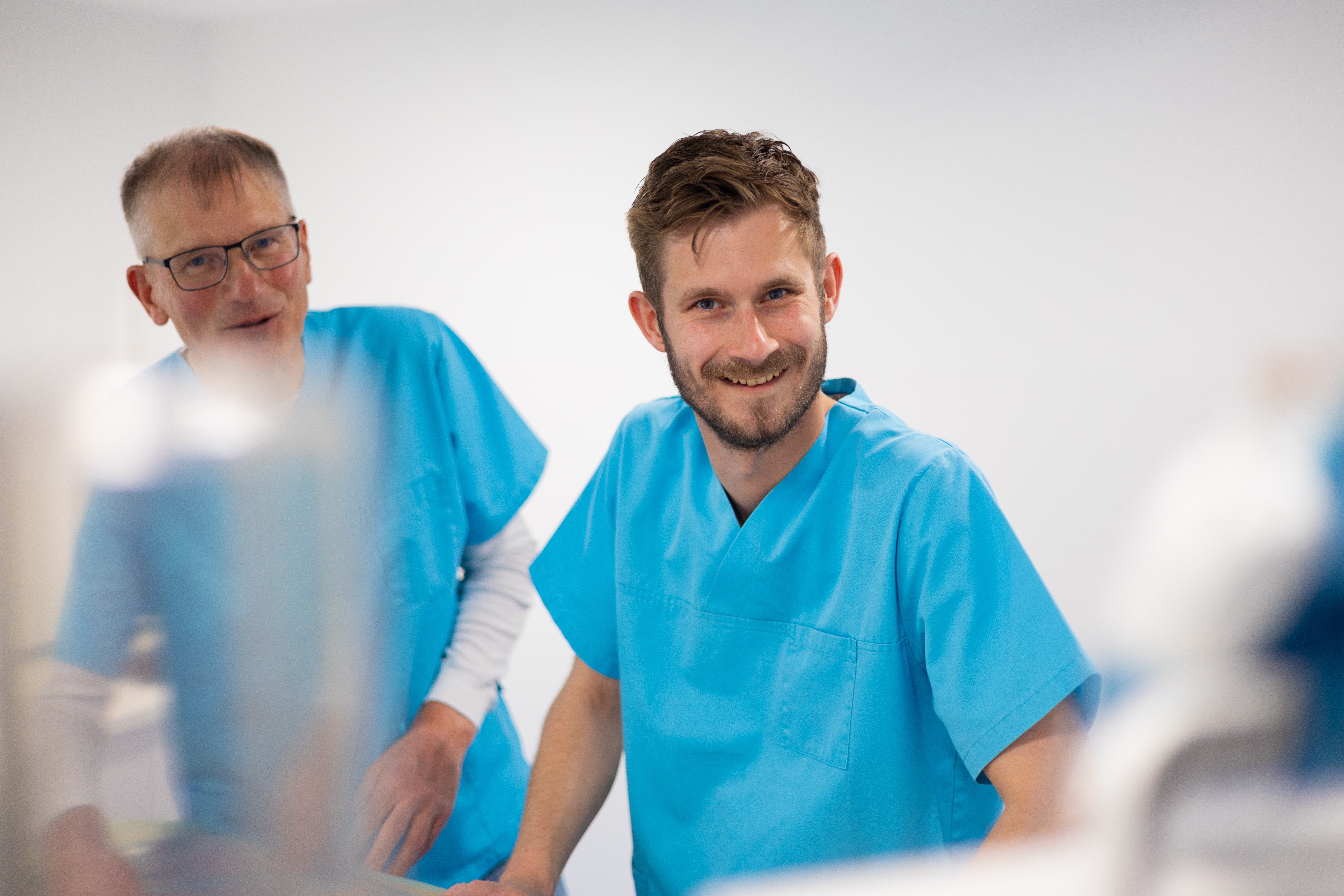 Zwei lächelnde Tierärzte in blauen OP-Hemden in einer hellen Tierarztpraxis.