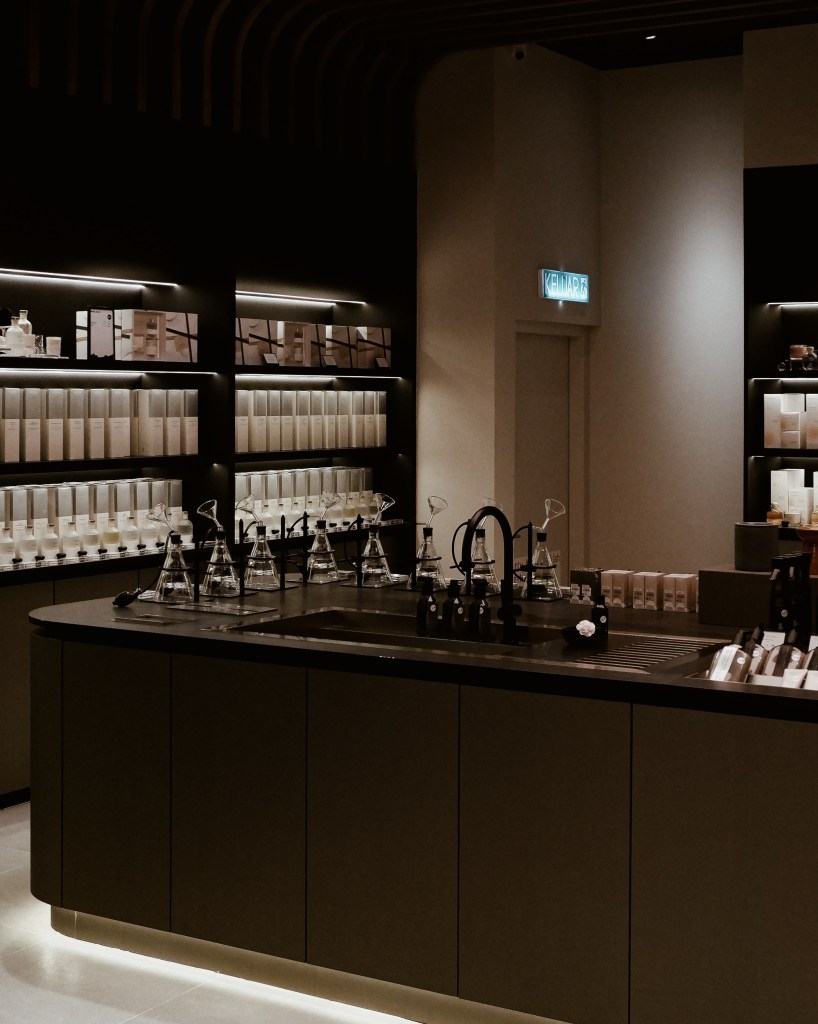 Interior view of HOOGA store in Damansara Heights featuring dark cabinetry, glass fragrance testing equipment, and a warm atmosphere with soft lighting.