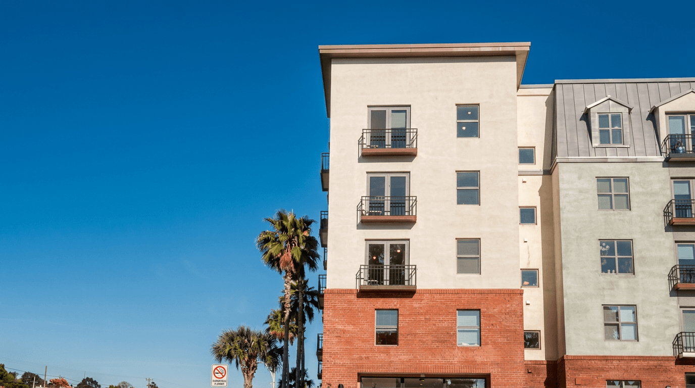 Facade of a modern building with balconies and palm trees under a blue sky.