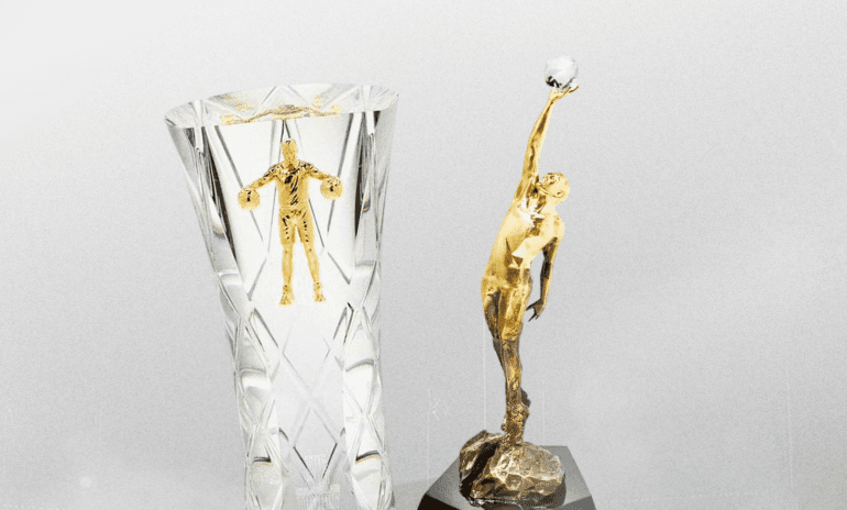 Man in dark grey suit holding NBA Rookie Award crystal trophy with gold basketball player figurine on top, smiling against grey background