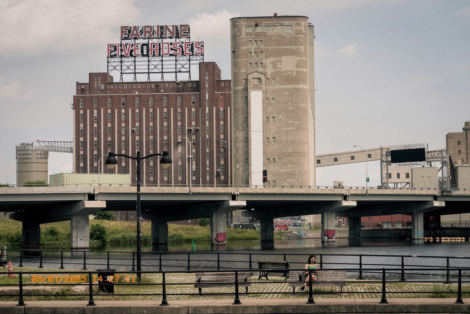 Ancienne usine Farine Five Roses à Montréal avec une femme assise au bord du canal.