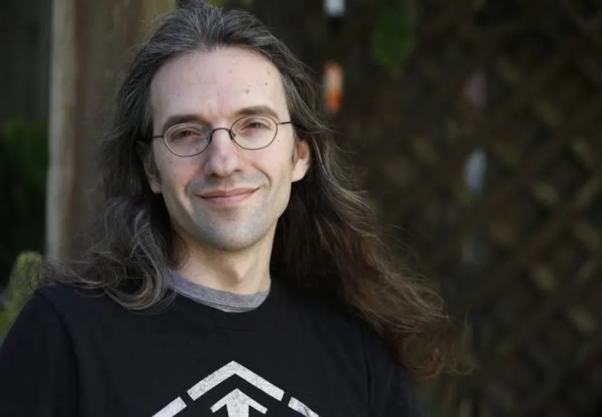 Author Alexander Freed's headshot in a black t-shirt in from of a blurred outdoor background.