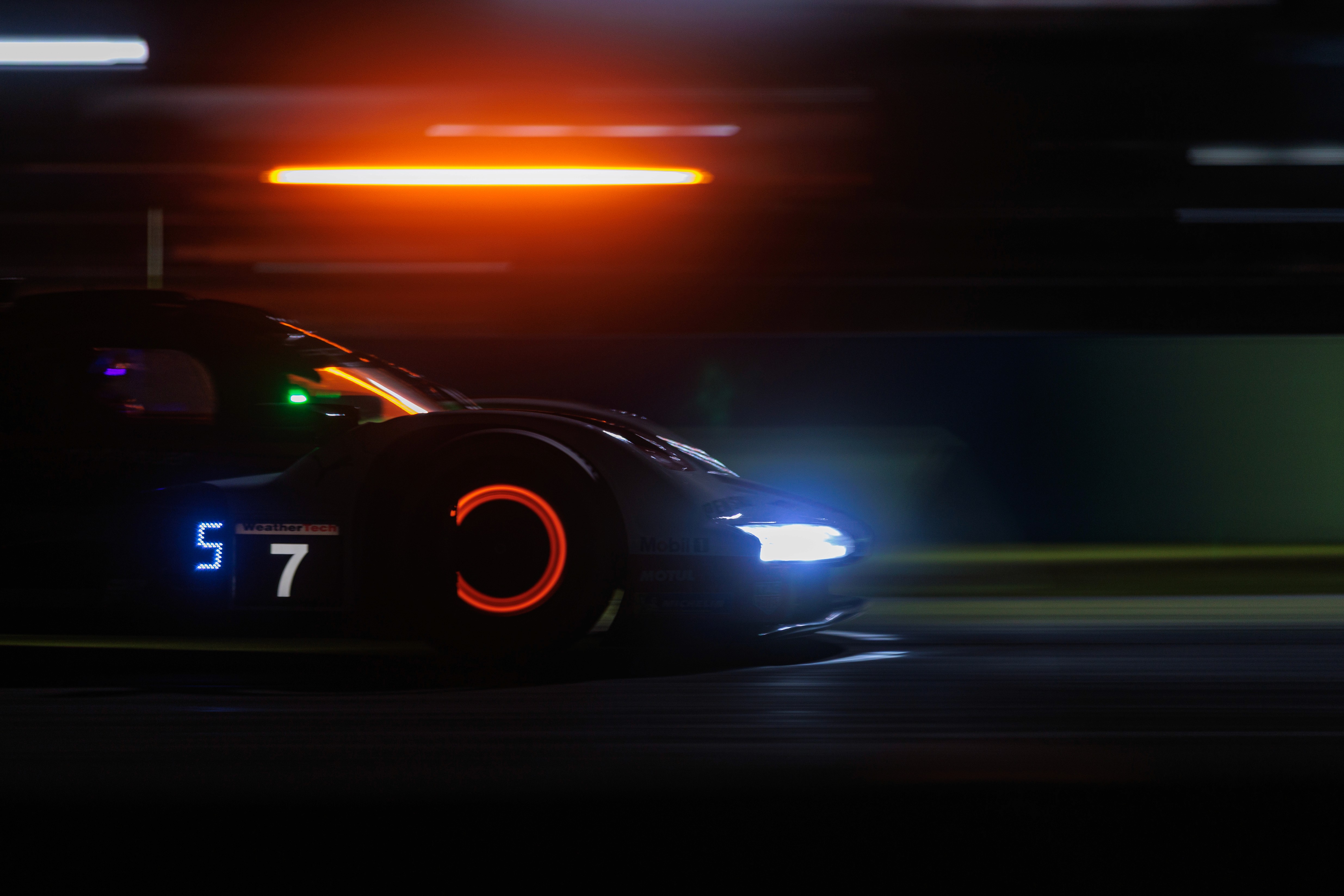 A race car speeds down a dimly lit track at night, with bright headlights illuminating the path ahead.