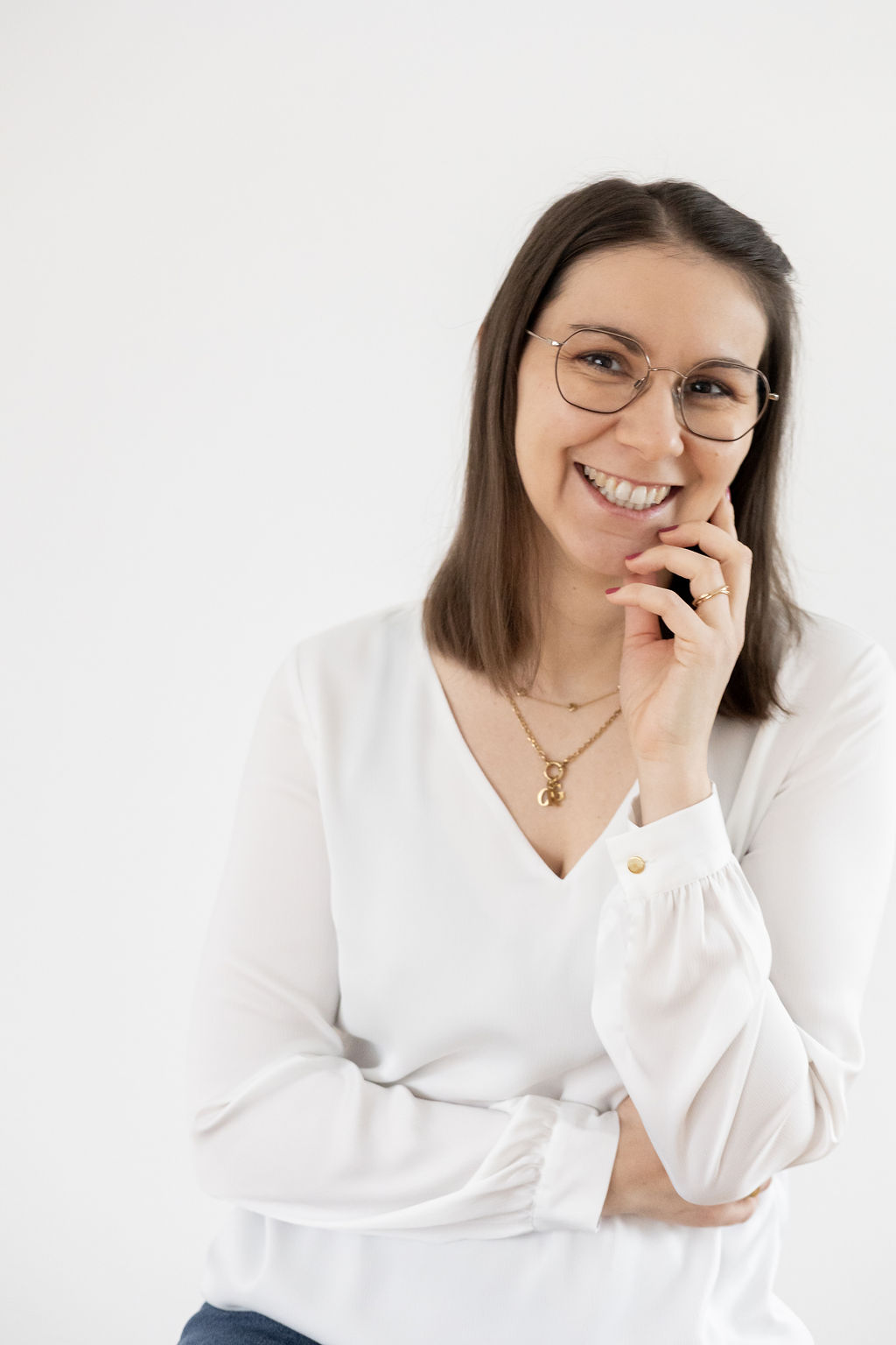 Smiling female therapist with short gray hair, wearing a brown top and a purple shawl, surrounded by a cozy background.
